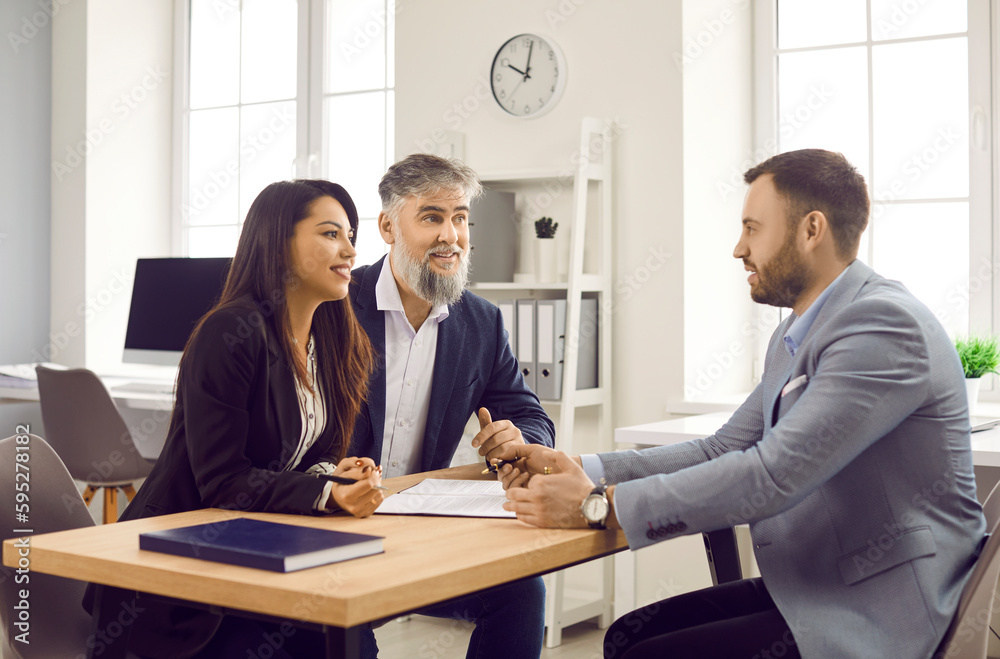 Estate agent or legal adviser talking to clients. Man and woman sitting at desk and having discussion with realtor or bank manager. Team of business partners discussing deal during meeting in office Estate agent or legal adviser talking to clients. Man and woman sitting at desk and having discussion with realtor or bank manager. Team of business partners discussing deal during meeting in office