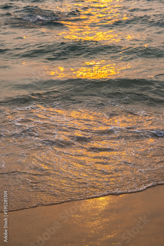 Sea wave foam on sandy beach in sundown light  close up. Tropical summery background.