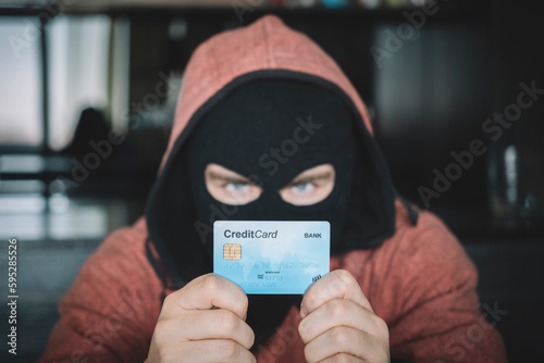 Photography A thief in a black mask holds a stolen bank card in his hands