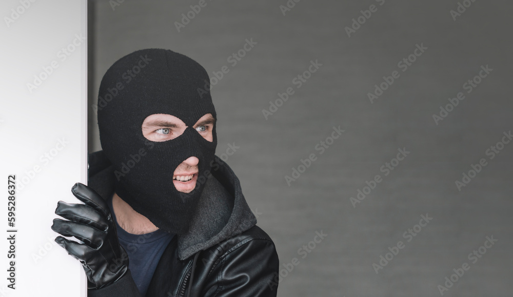 An evil thief in mask looks out from behind a white board. Space for text and design. copy space. the surprised bandit looks away An evil thief in mask looks out from behind a white board. Space for text and design. copy space. the surprised bandit looks away