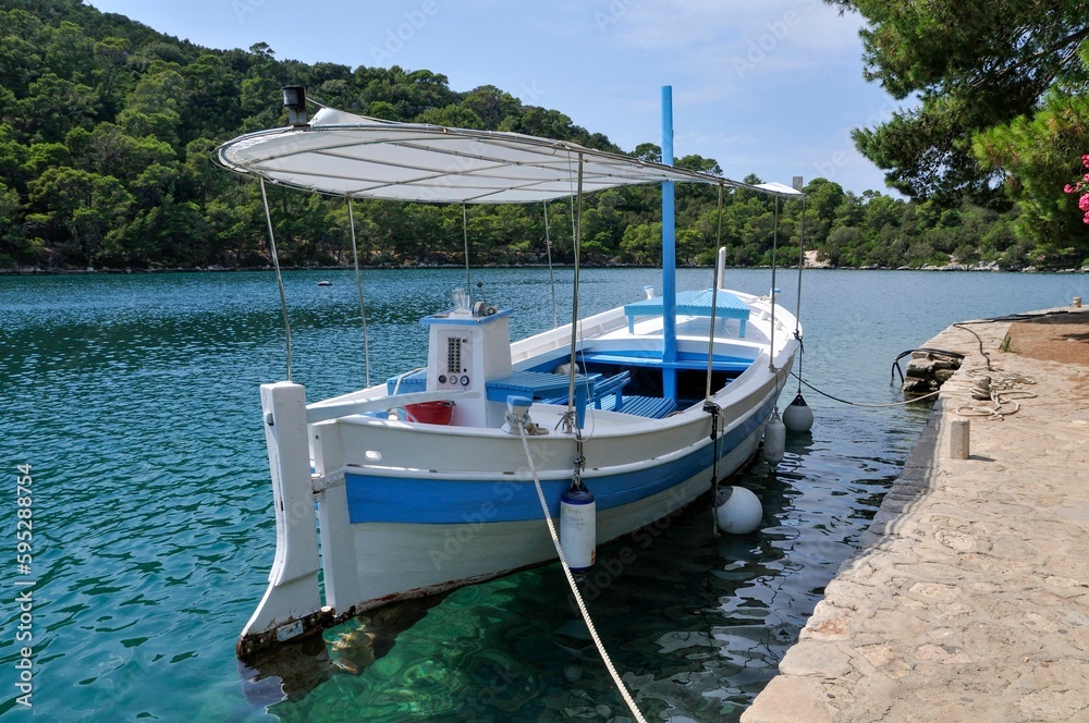 Small boat with blue and white stripes secured to a wooden pier on a sunny lake