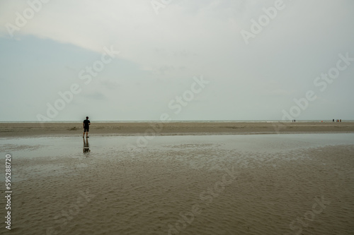 landscape of Bakkhali sea shore. Silhouette of a man walking on the beach at low tide