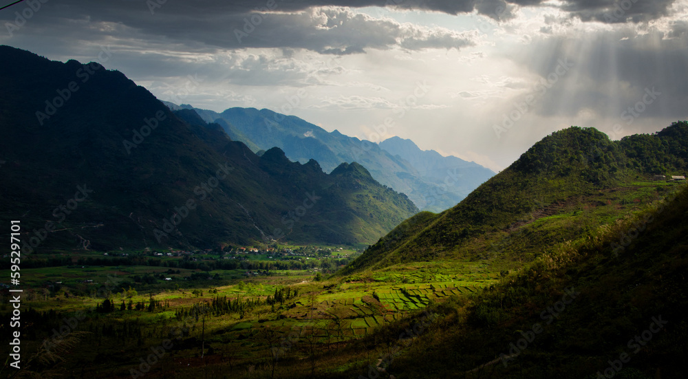 The sun's rays are going through the clouds, illuminating a valley of rice fields in Vietnam.
