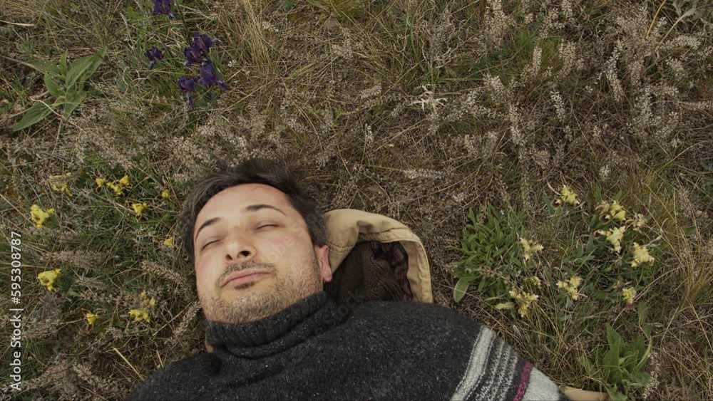 An unshaven handsome middle aged man with closed eyes lies on the grass among the first wildflowers and enjoys nature An unshaven handsome middle aged man with closed eyes lies on the grass among the first wildflowers and enjoys nature