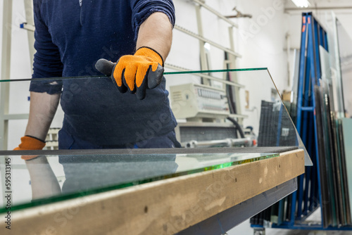 A glazier in a glass factory removes a large piece of glass from a table