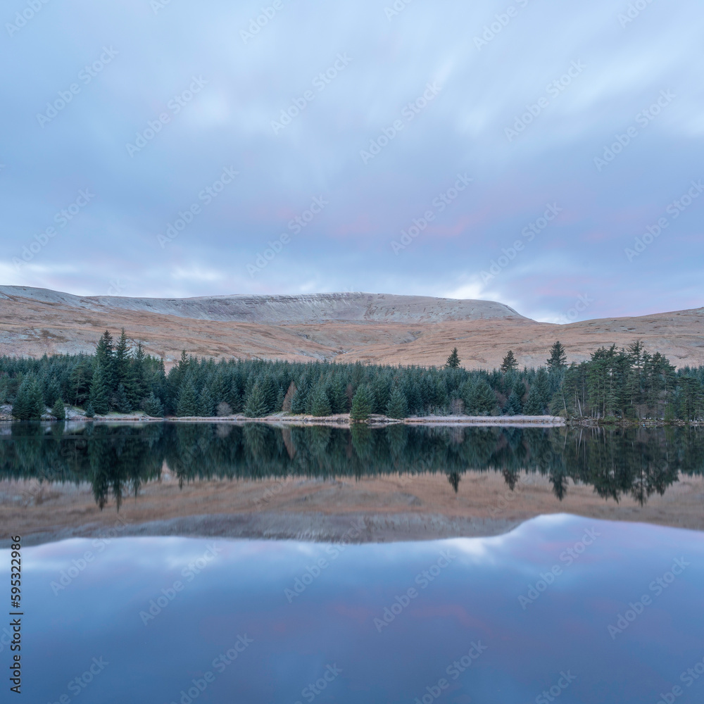 Mountains and treeline, reflected in the calm waters of a mountain lake. Brecon Beacons