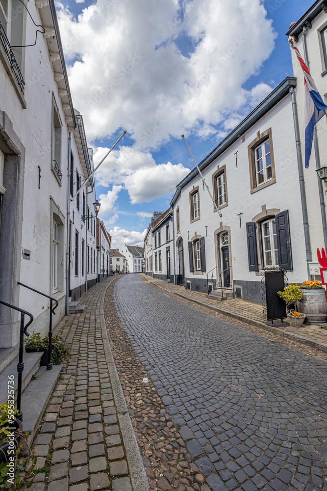 Urban landscape of a narrow cobbled street and sidewalks between buildings with white walls against blue sky and clouds, sunny day in old Dutch town of Thorn, Midden-Limburg in the Netherlands