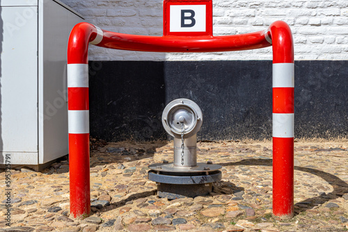 Fire hydrant between a red metal barrier with white lines against black and white wall, B for Brandweer, means: fire brigade, cobbled street in a Dutch village. Fire safety concept photo