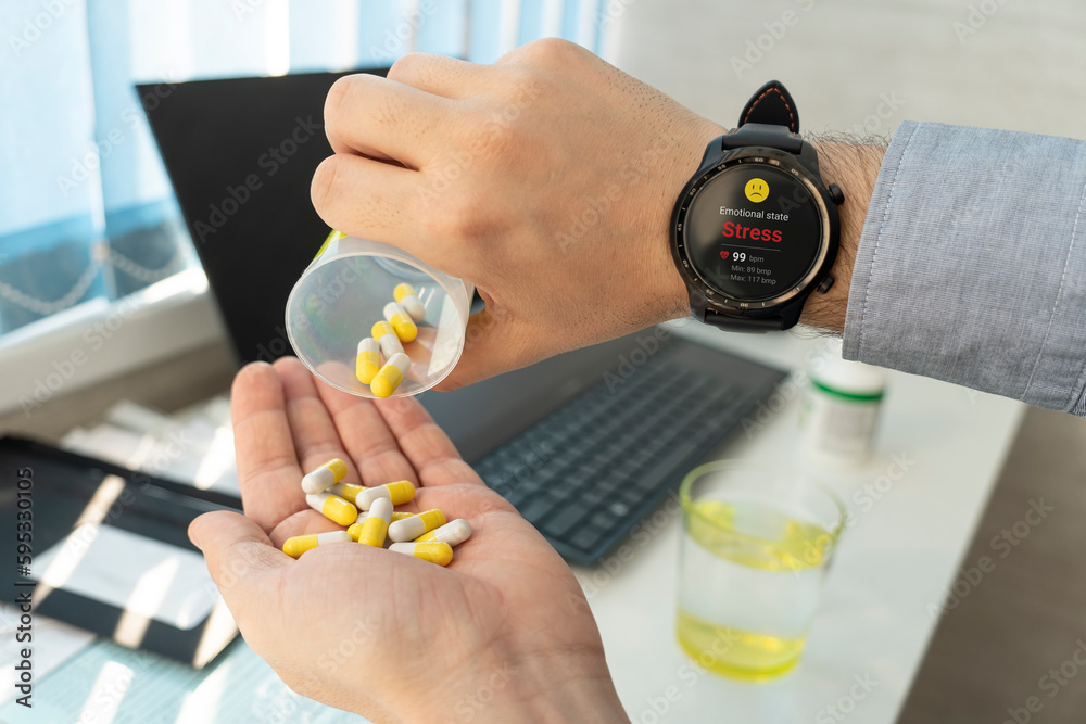 Obraz premium Sick mature man taking pills at work. stress and overwork at work concept. sick businessman drinks sedative pills. The smart watch shows emotional state on screen. Taking antidepressants at work.