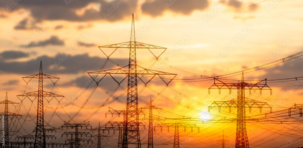 high voltage towers with power line grid for transmission of electricity, beautiful industrial landscape with bright sunset light in germany, Europe