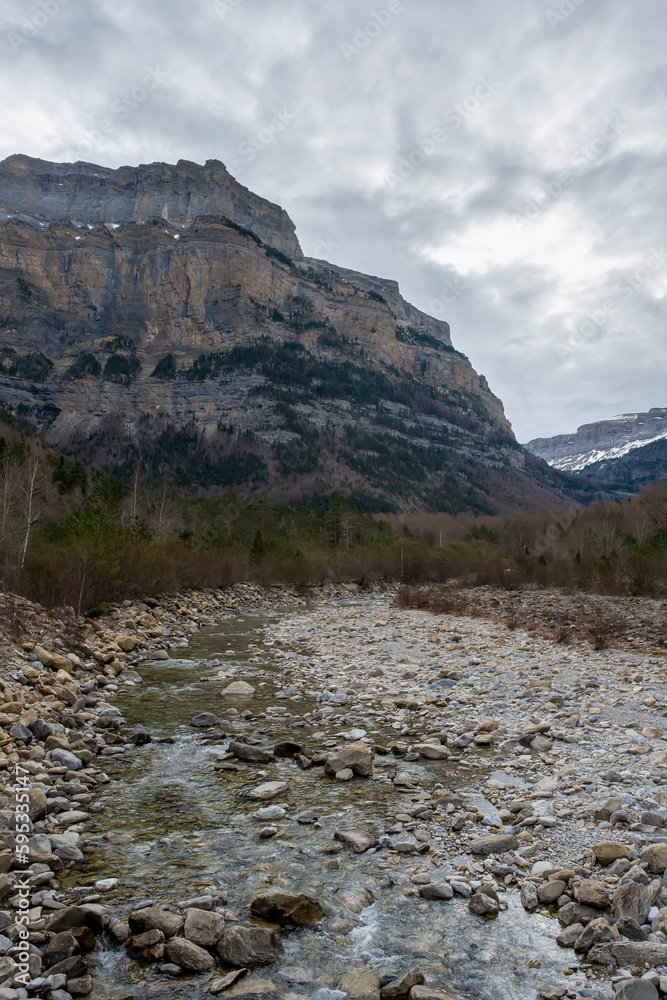 A mountain river flows through a valley between large rocky mountains, Arazas river, Ordesa y Monte Perdido National Park, Huesca, Aragonese Pyrenees, Spain