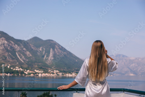 Fototapeta Naklejka Na Ścianę i Meble -  Young woman in silk robe standing on the balcony with sea on background