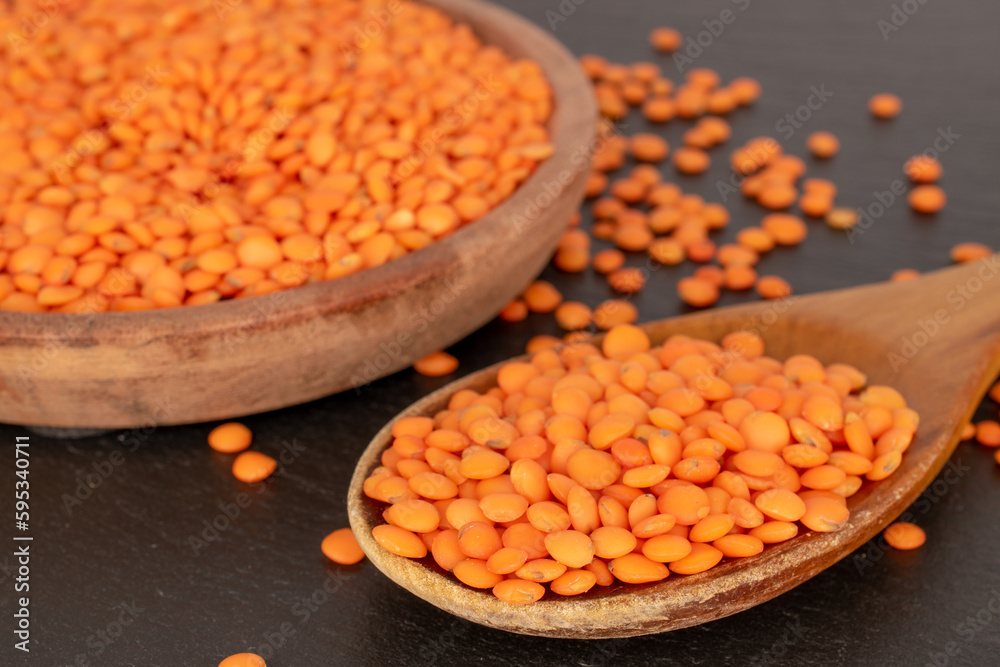 Red lentils with wooden spoon and saucer on slate stone, macro. Red lentils with wooden spoon and saucer on slate stone, macro.