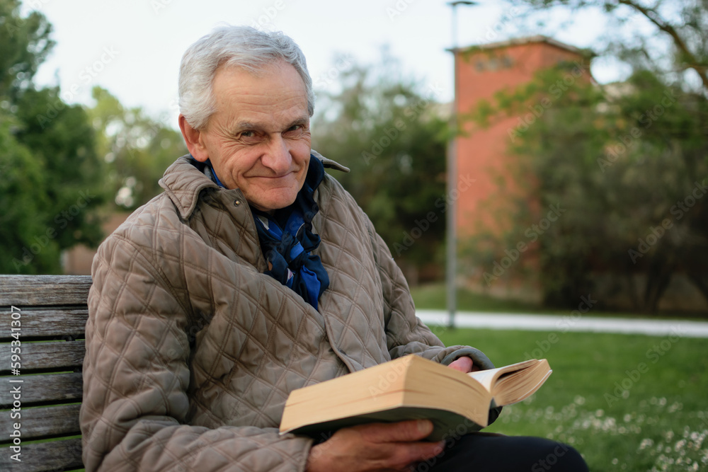 Old man with gray hair reading a book sited on an bench. Old man with gray hair reading a book sited on an bench.