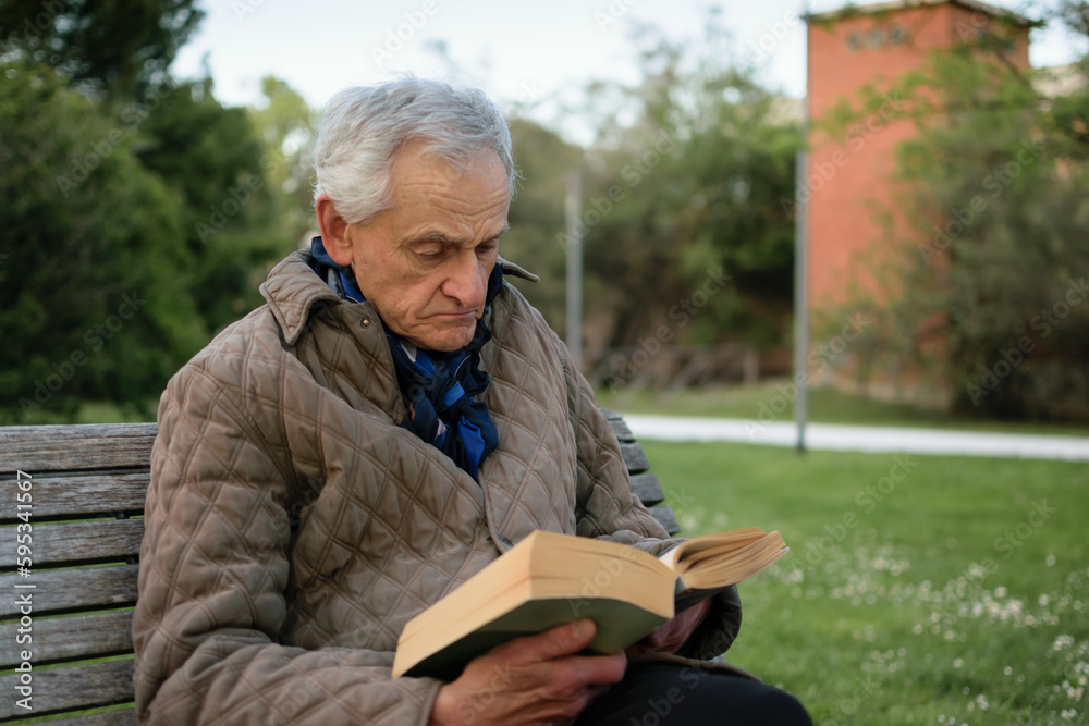 Old man with gray hair reading a book sited on an bench. Old man with gray hair reading a book sited on an bench.