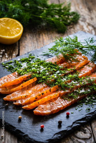 Gravlax - fresh marinated salmon slices in salt and dill on black plate on wooden table 