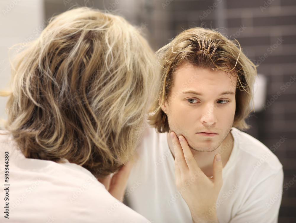 young man looking in the mirror,combing his hair,looking at problems on face. young man looking in the mirror,combing his hair,looking at problems on face.