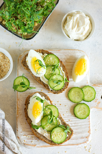 Cottage cheese sandwiches on whole grain bread with half an egg and cucumber on a wooden board on the table top view