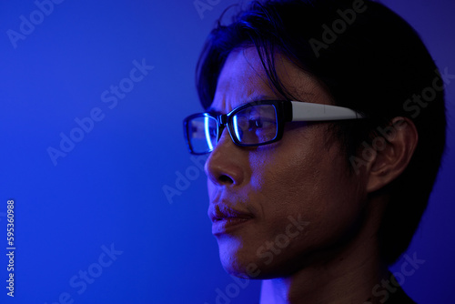 Face of serious man in glasses standing in blue light and looking away