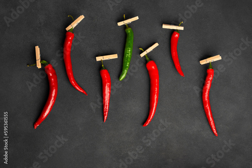 Composition of red and green peppers hung on pegs, one stand out. Isolated on black or dark gray background. Flat lay, top view.