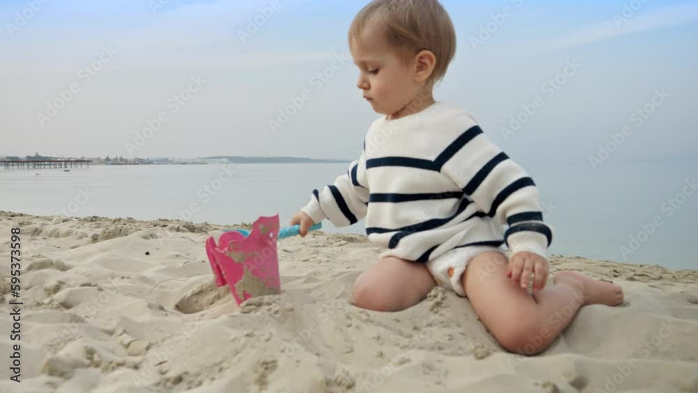 Toddler boy happily playing on the beach and digging sand with a shovel. Joy, excitement, and freedom of a family vacation, journey, and weekend