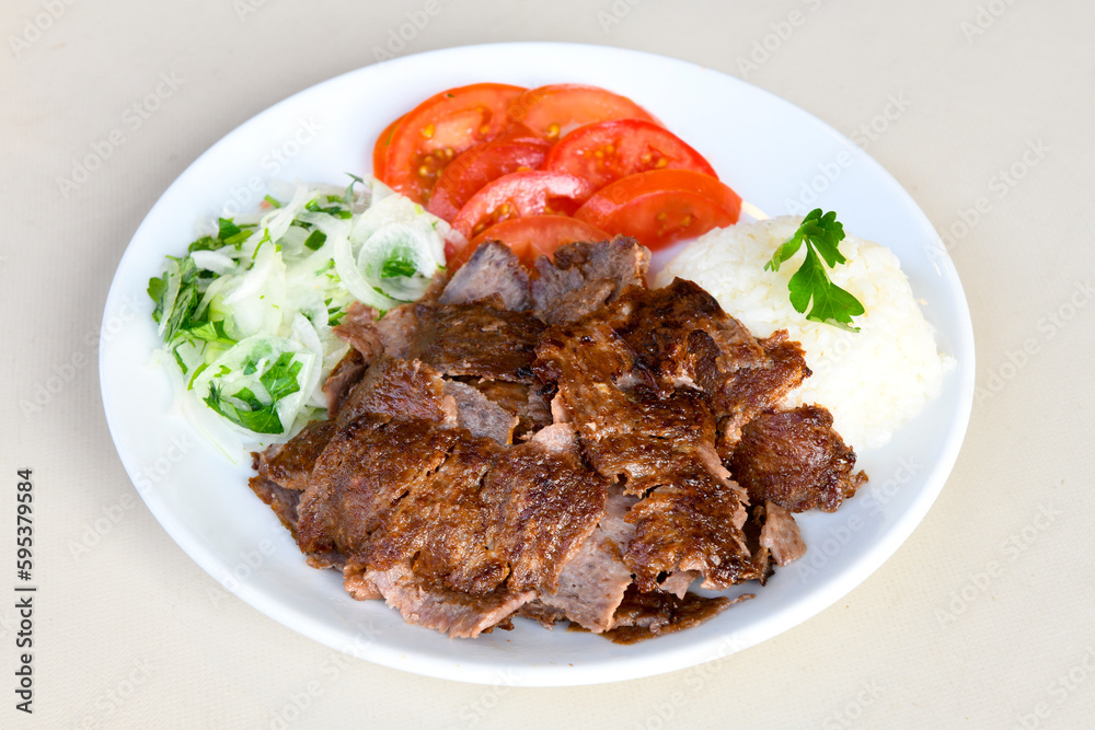 Turkish and Arabic Traditional Ramadan doner kebab with tasty tomato sauce and rice or turkish pilav in white plate on wood table background. ( Pilav ustu doner)