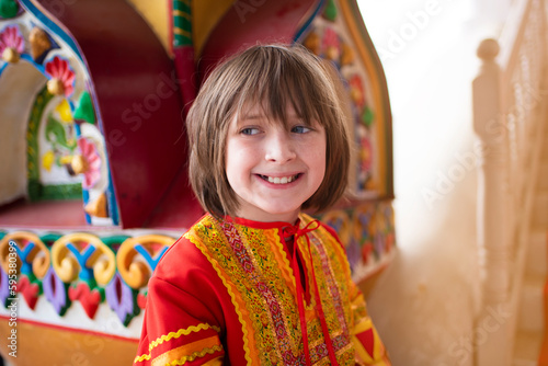  a happy boy in a Russian national bright red-orange costume near the Russian national multi-colored Terem building.