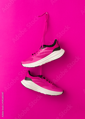 Pair of stylish pink sneakers hanging on color red background. Fashionable stylish sports casual shoes. Modern creative minimalistic layout with footwear. Mock up for design advertising for shoe store