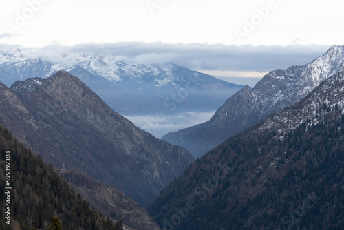 Champorcher Valley (Aosta Valley, Italian Alps) in winter, snow covered mountains, forest, low clouds and haze in the valley