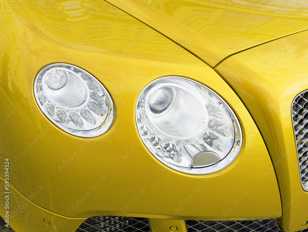 Particle view of yellow brand new modern luxury sport car parked outdoors. Headlights and hood of sport yellow car. Car detail