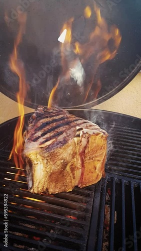 Traditional barbecue chianina bistecca alla Fiorentina beef steak grilled as close-up on a charcoal grill with fire and smoke – video and audio