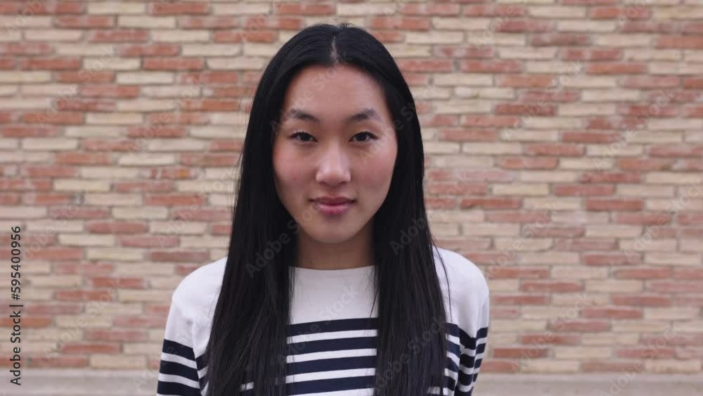 Young adult chinese woman looking at camera standing over brick background wall. Asian people concept Young adult chinese woman looking at camera standing over brick background wall. Asian people concept