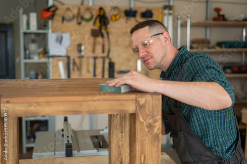 Male carpenter finishing work on wooden table in workshop. 