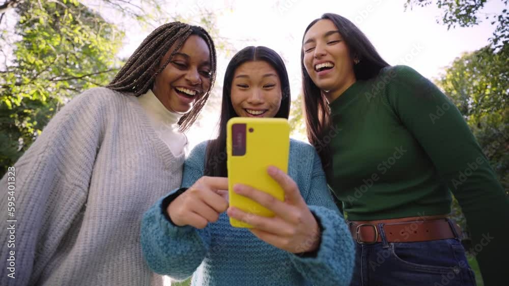 Three young women using phone while having fun in the park and laughing ...