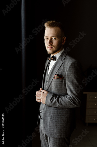 a young and handsome groom in a suit and a vest with a bow tie is assembled for the wedding. successful entrepreneur marries. successful man. portrait of the groom