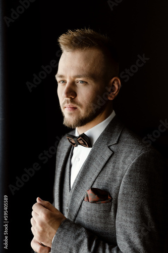 a young and handsome groom in a suit and a vest with a bow tie is assembled for the wedding. successful entrepreneur marries. successful man. portrait of the groom