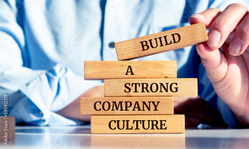 Close up on businessman holding a wooden block with a "Build a strong company culture" message