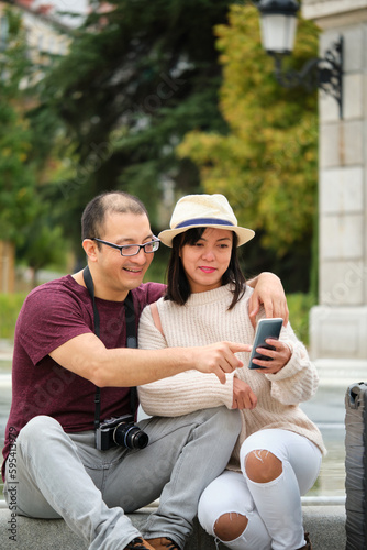 Multiracial couple of tourists consulting a city guide in their smartphone. Sightseeing in Madrid, Spain.