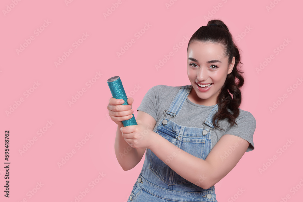 Young woman blowing up party popper on pink background, space for text
