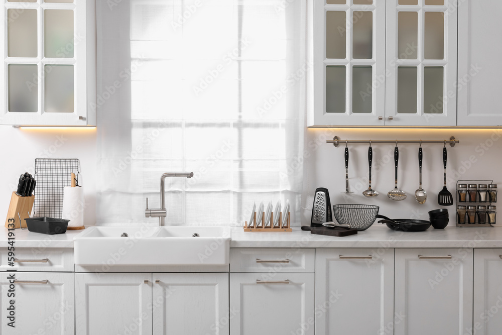 Set of different utensils near sink on countertop in kitchen Set of different utensils near sink on countertop in kitchen