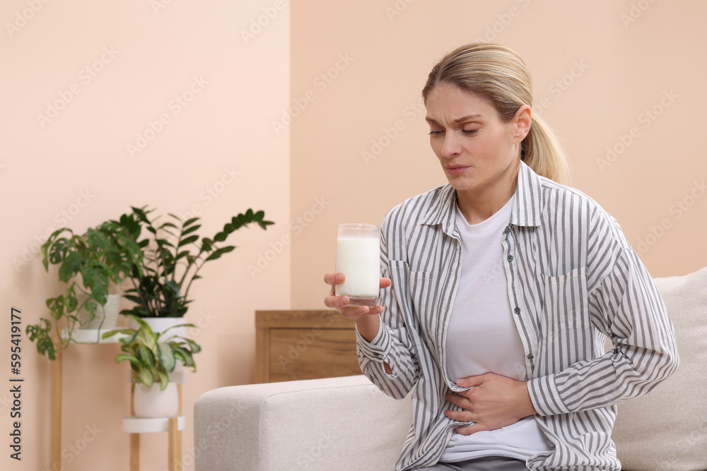 Woman with glass of milk suffering from lactose intolerance at home, space for text Woman with glass of milk suffering from lactose intolerance at home, space for text