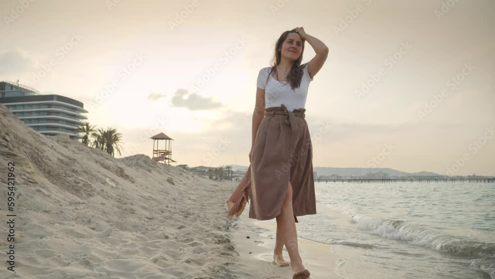 Happy smiling woman in long skirt walking on the sandy sea beach at sunset. Concept of happiness, travel, journey, trip, tourism and holiday Happy smiling woman in long skirt walking on the sandy sea beach at sunset. Concept of happiness, travel, journey, trip, tourism and holiday
