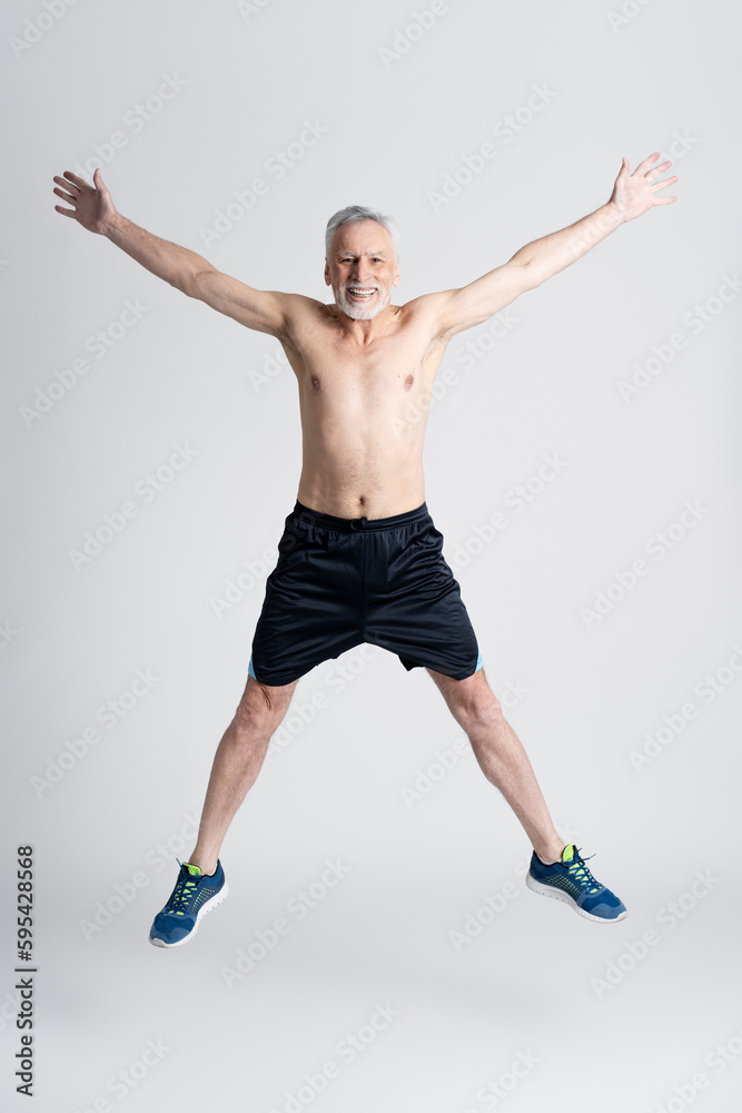 Smiling senior man with naked torso jumping, isolated on white background. Athletic senior man Smiling senior man with naked torso jumping, isolated on white background. Athletic senior man