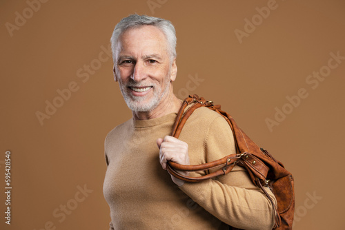 Portrait of modern senior man holding leather bag on shoulder isolated on beige background photo