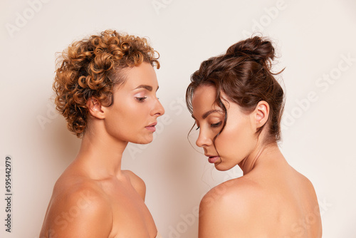 Medium close-up shot of two girls on the white backdrop, the curly one stands in profile, the second one faces to her, beauty concept, copy space, high quality photo