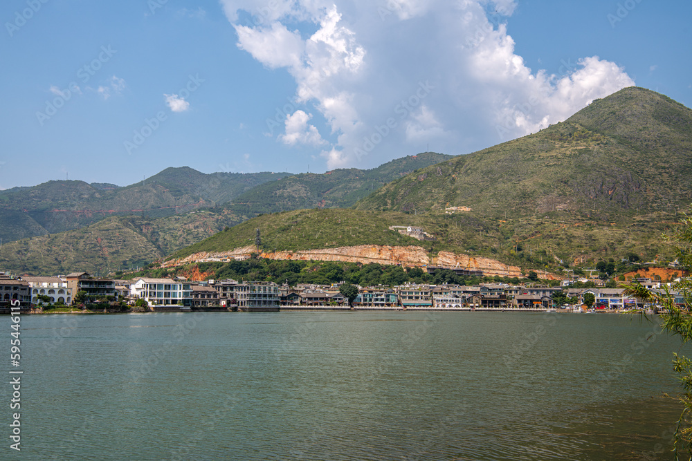 mountains and inn houses along the blue Erhai lake in Shuanglang Yunnan China. Symmetrical reflection in peaceful water. Sunny blue sky white clouds. Famous tourist attraction, copy space for text