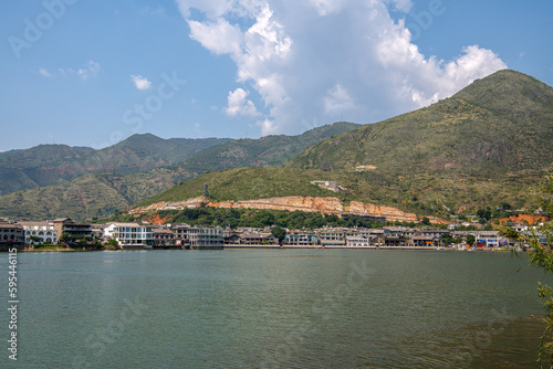 mountains and inn houses along the blue Erhai lake in Shuanglang Yunnan China. Symmetrical reflection in peaceful water. Sunny blue sky white clouds. Famous tourist attraction, copy space for text