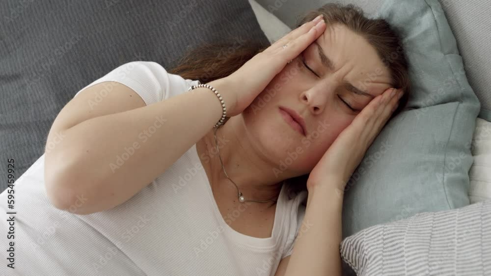 Portrait of young owman lying in bed and suffering from headache. Concept of healthcare problems, pain relief and hangover Portrait of young owman lying in bed and suffering from headache. Concept of healthcare problems, pain relief and hangover