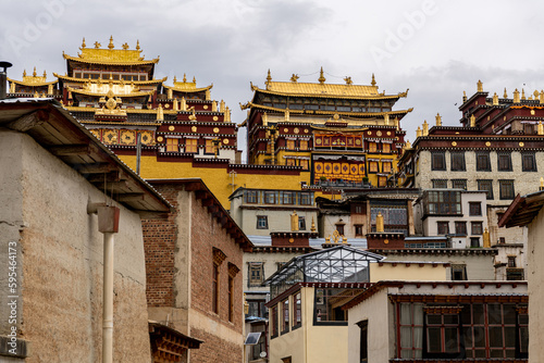 The buildings of Buddhist Ganden Sumtseling Monastery (Songzanlin Monastery) in Shangri-La, Yunnan with the sun shining on the buildings of the manastery and moody dramatic sky photo