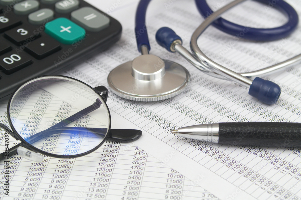 Cost of medicine and health insurance. Black calculator, pen, eyeglasses and stethoscope on financial data. Cost of medicine and health insurance. Black calculator, pen, eyeglasses and stethoscope on financial data.